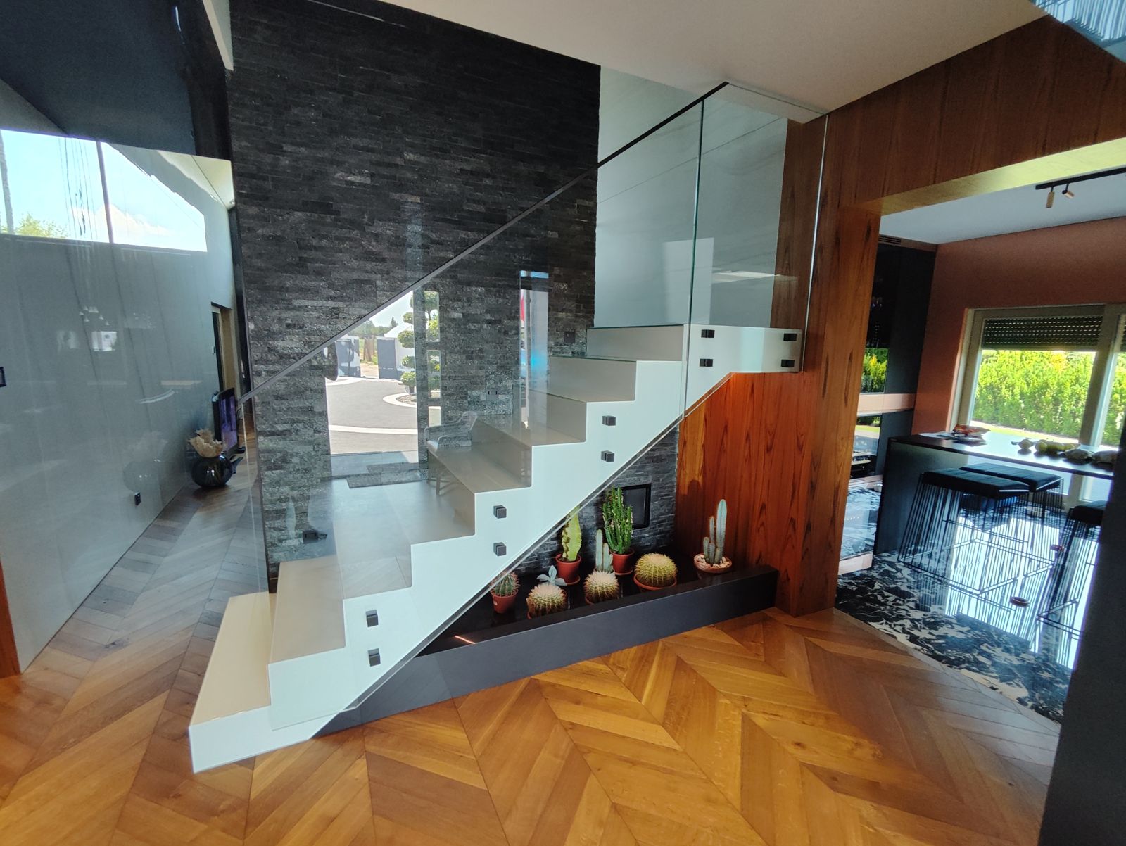Schody w salonie ze szklaną balustradą, w tle ściana z kamienia